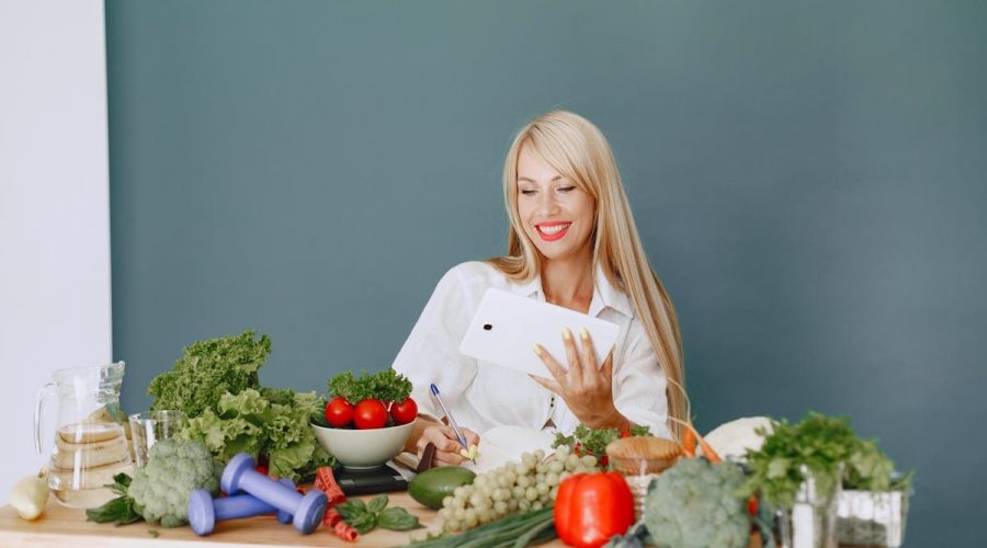Woman using a tablet surrounded by fresh vegetables at a table, showcasing healthy lifestyle and technology.